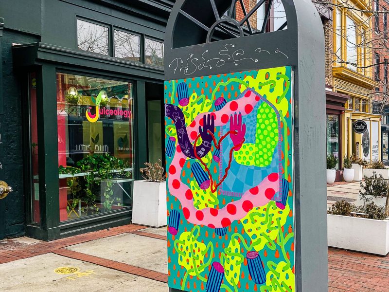A multicolored artwork on display on a kiosk outdoors.