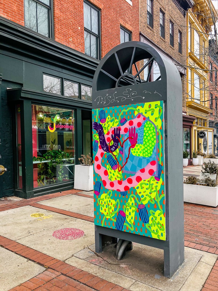 A multicolored artwork on display on a kiosk outdoors.