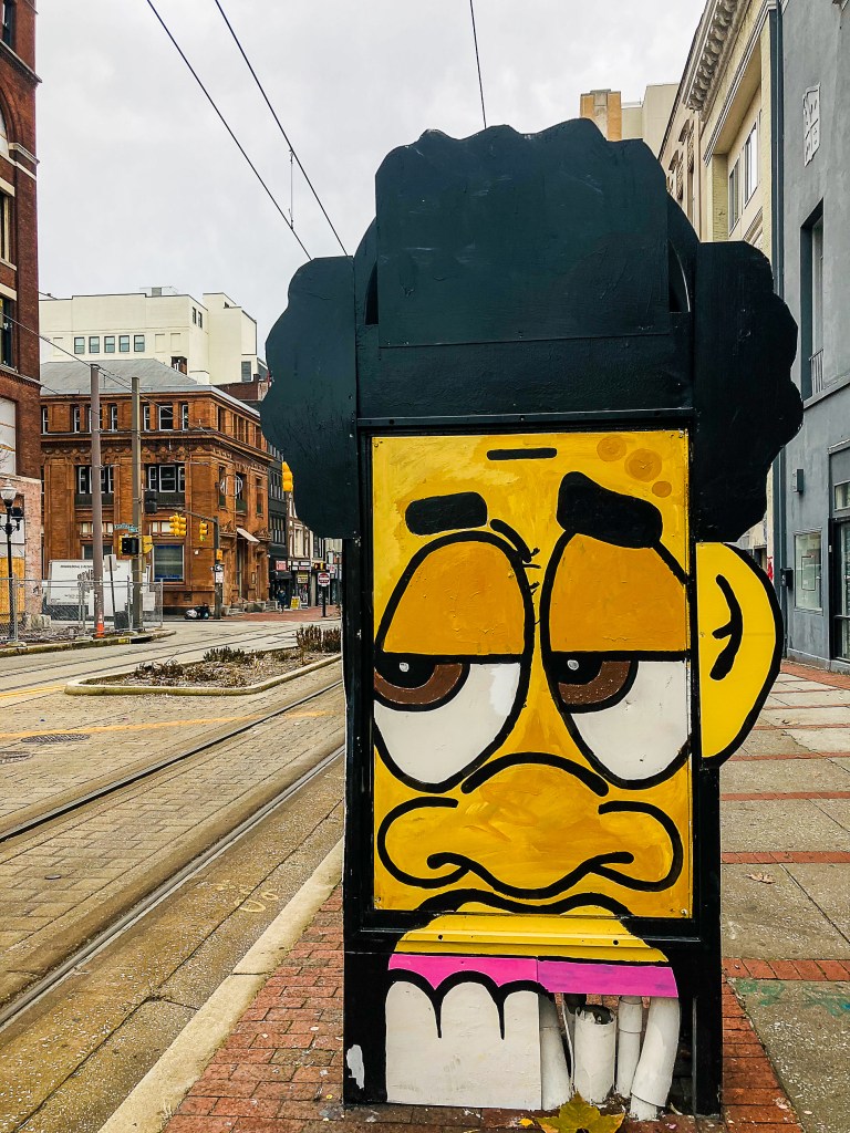 An outdoor kiosk with a painted image of a yellow cartoonish figure on display on howard street.