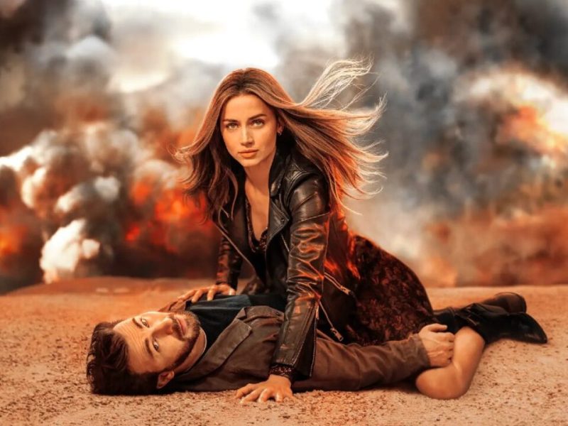 A still from a film where two characters look at the camera, there is smoke in the background.