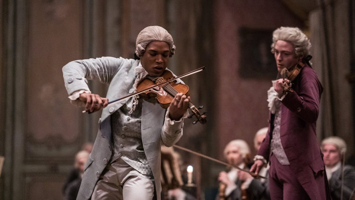 Film still from Chevalier, two men are playing insturmetns in period costumes, the main character has brown skin and a wig and is playing the violin.