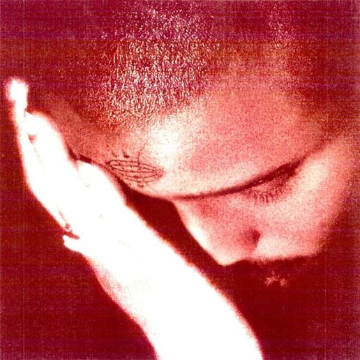 A photo of a person with short hair holding their head. They have a tattoo on their forehead.