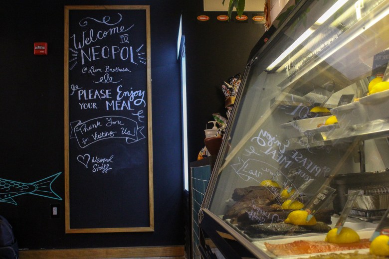 Neopol Savory Smokery's Hollins Street location, a display case, and a chalkboard that reads: Welcome to Neopol @ lion brothers, please enjoy your meal, thank you for visiting us. Heart, Neopol Staff."