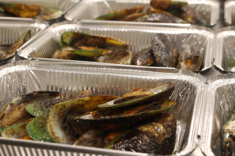 A close up photograph of smoked mussels in a silver container.