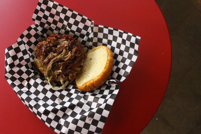 A photograph of a pulled pork sandwich on a red table top.