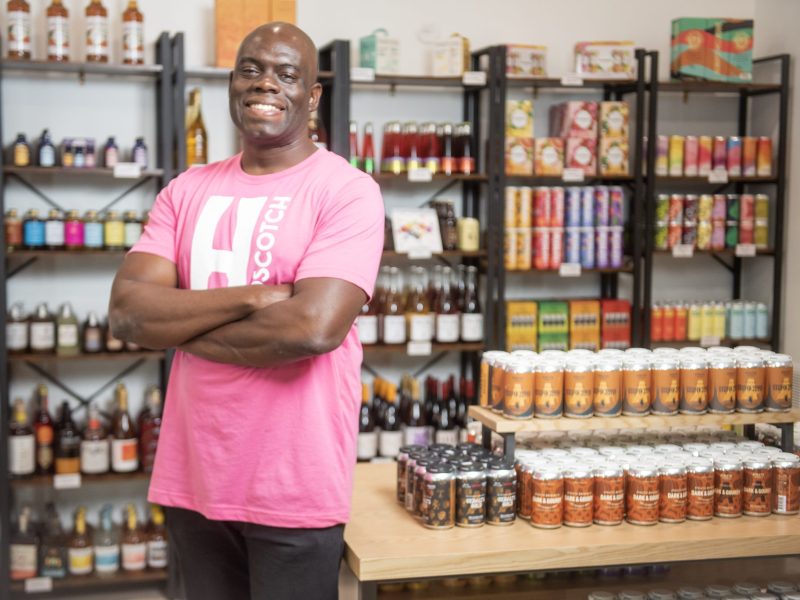 A man with brown skin wearing a pink shirt smiles in his store.