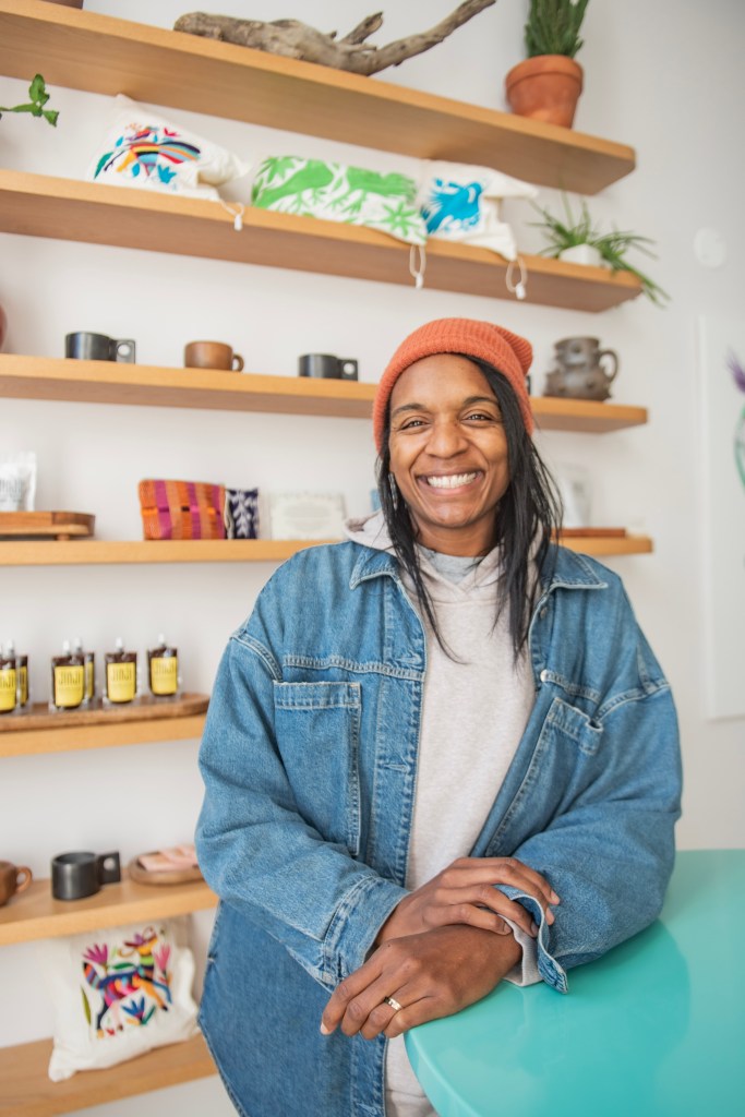 A photograph of a woman with brown skin smiling, she is wearing a orange hat.