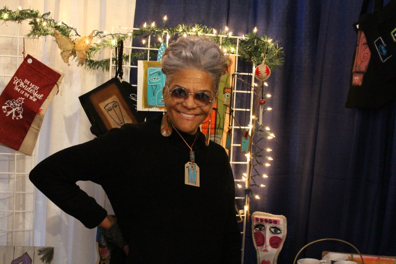 A woman with brown skin and grey hair smiles in her booth. 