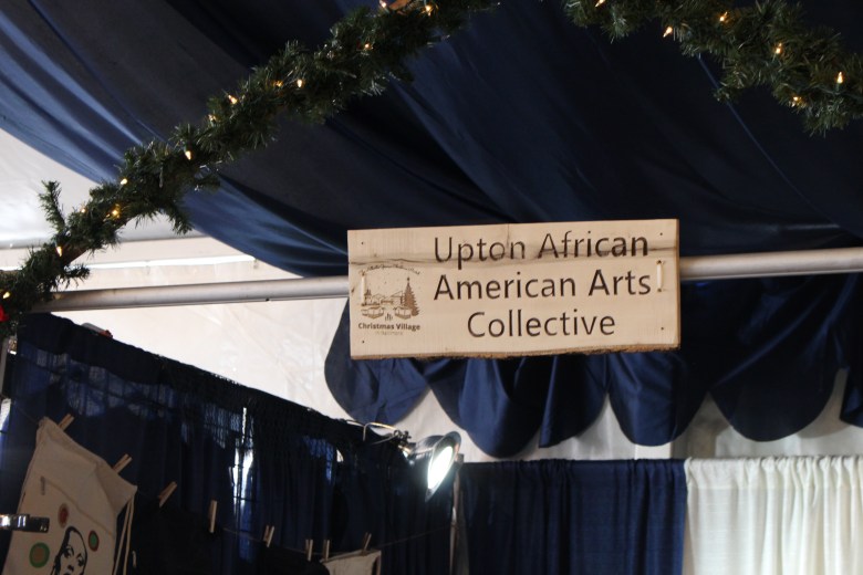 A sign reads "upton african american arts collective" at a both at the Baltimore Christmas village.