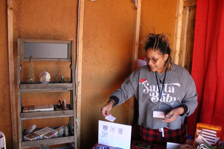 A woman with brown skin wearing a grey sweatshirt prepares her booth for at the Baltimore Christmas Village.