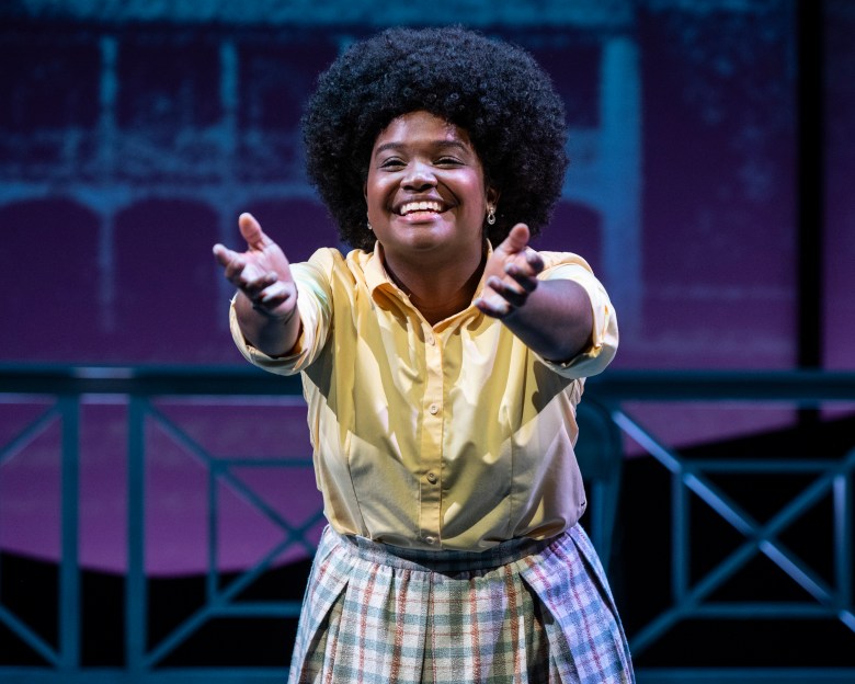 A person with brown skin performs on a stage. 