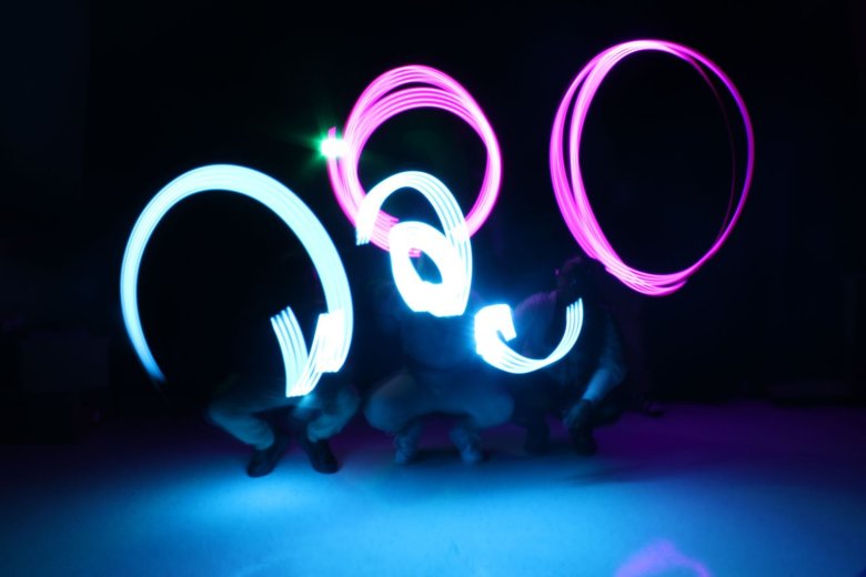 Swirls of green and blue light. You can see the feet of three people crouching below the lights.