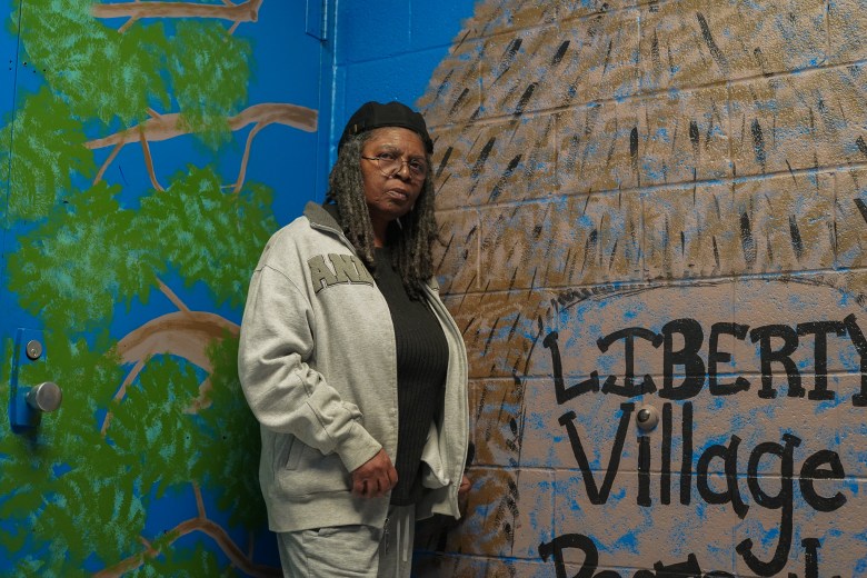A Black woman stands against a brightly painted wall.