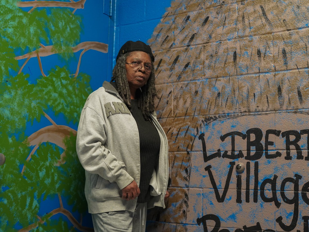 A Black woman stands against a brightly painted wall.