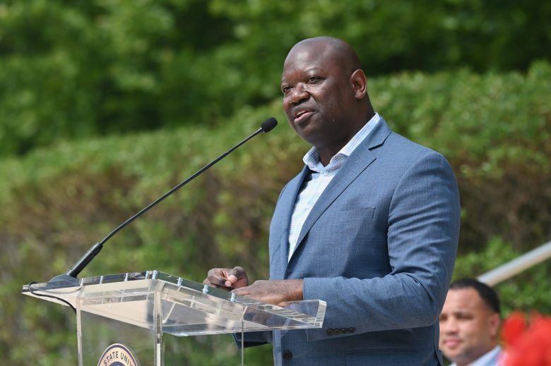 A man wears a blue shirt and blue jacket while speaking at a podium.