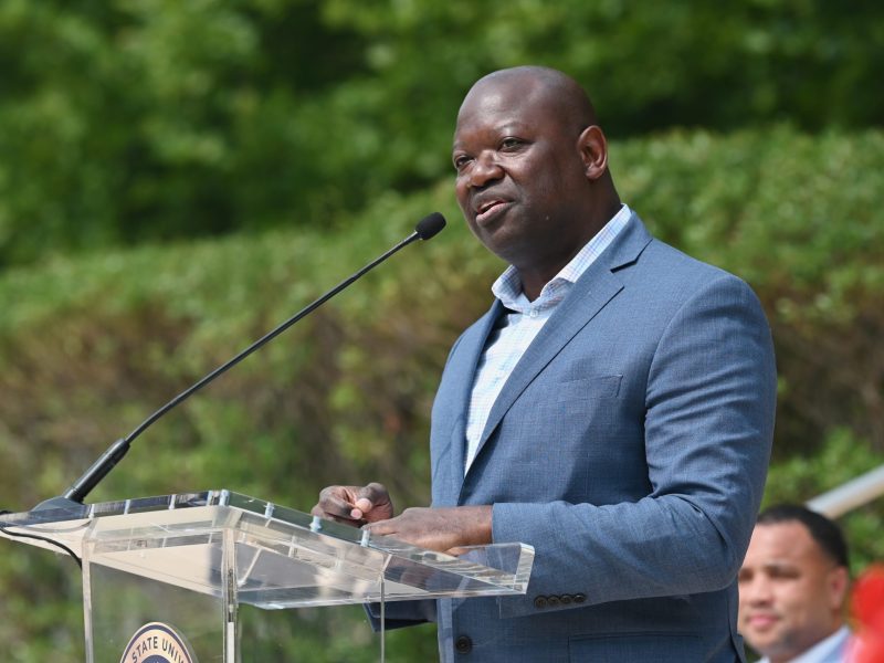 A man wears a blue shirt and blue jacket while speaking at a podium.