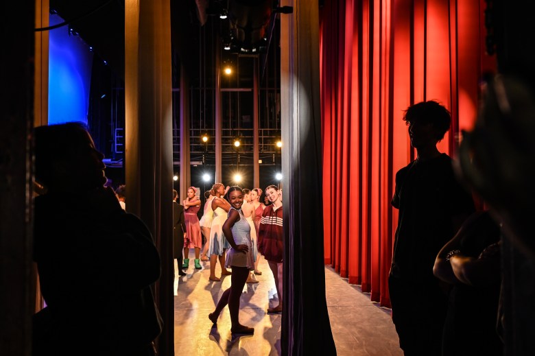 A student smiles at the camera from the stage. Other students stand in the background.