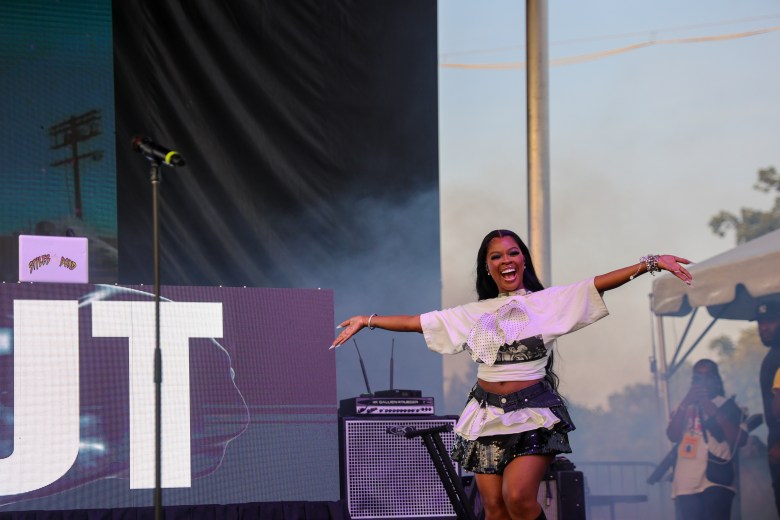 A smiling Black woman stands on a stage. She has on a black and white t-shirt and a black and white skirt.
