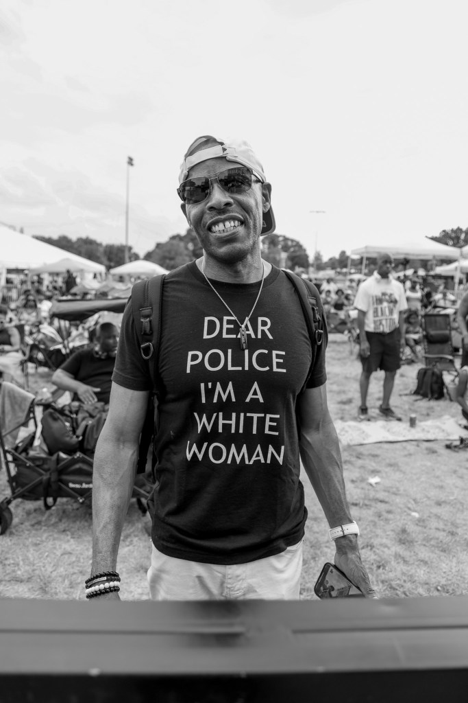 A man with brown skin smiles. he is wearing a black tshirt and sunglasses