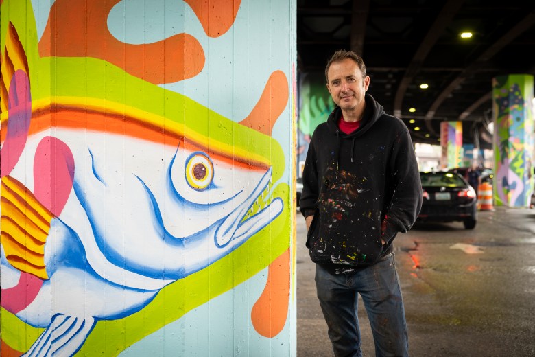 Andy Dahl stands to the right of a pillar he painted a large silver hake fish on as a tribute to Baltimore's lake trout dish.