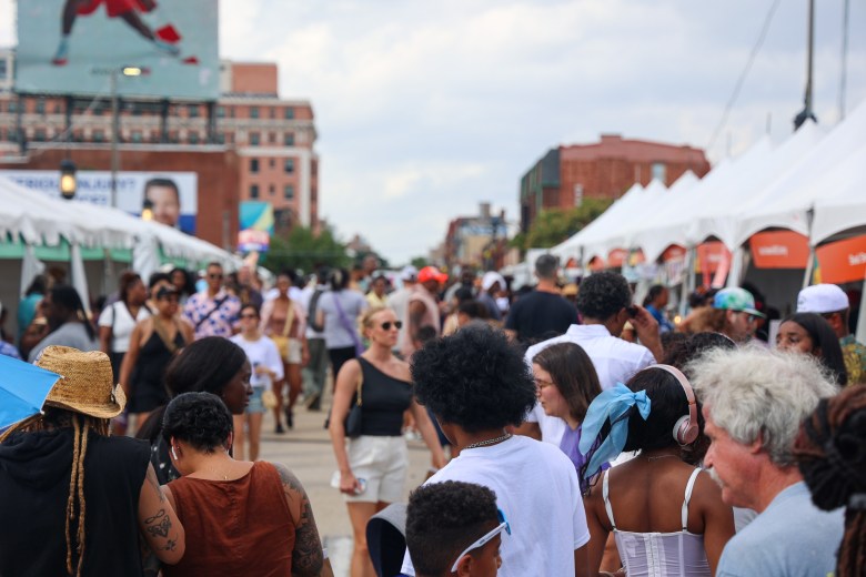 A crowd of patrons shopping through a selection of goods from a lane of tents