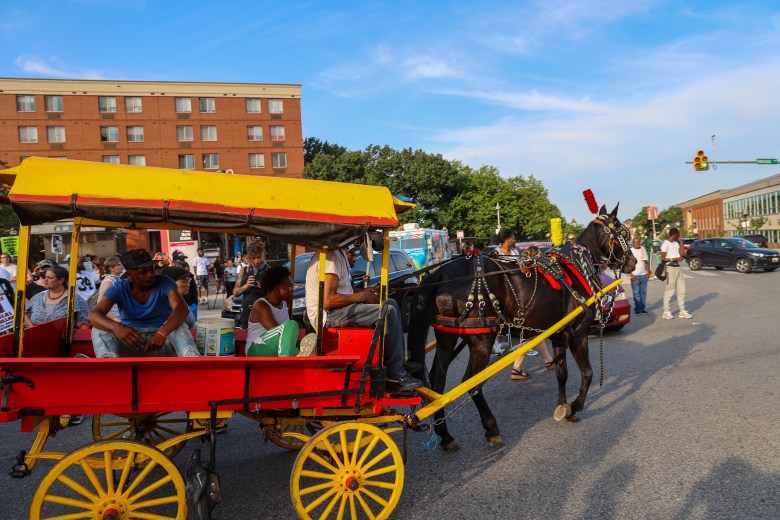 A brown horse pulls a red and yellow cart in Baltimore City.