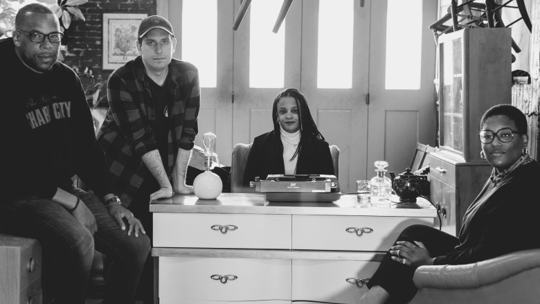 Photo of the Beat Staff, in black and white, photographed by Schaun Champion. Left to right: J. Brian Charles sitting, Brandon Soderberg leaning forward, Lisa Snowden sitting at a desk, and Teri Henderson sitting in a chair.