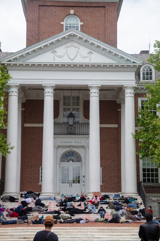 Protesters stage a die-in in front of Gilman Hall at Johns Hopkins University. Photo shows people lying down on the steps of the building.