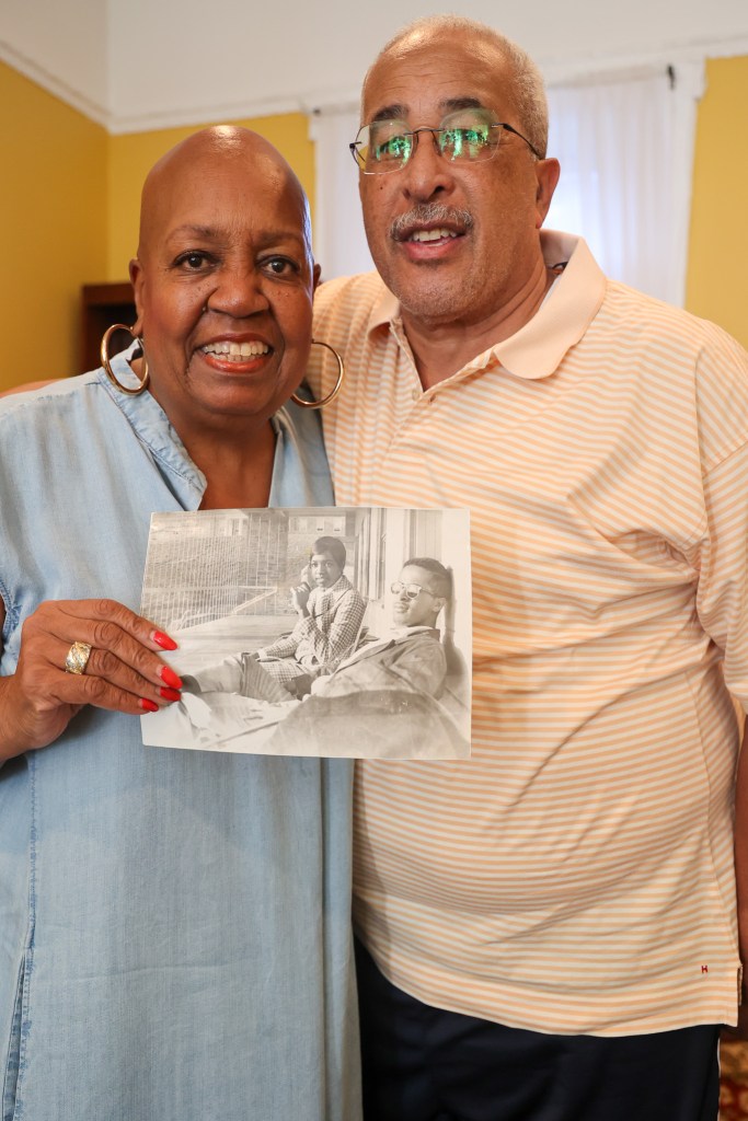 two people with brown skin embrace and hold a black and white photograph.