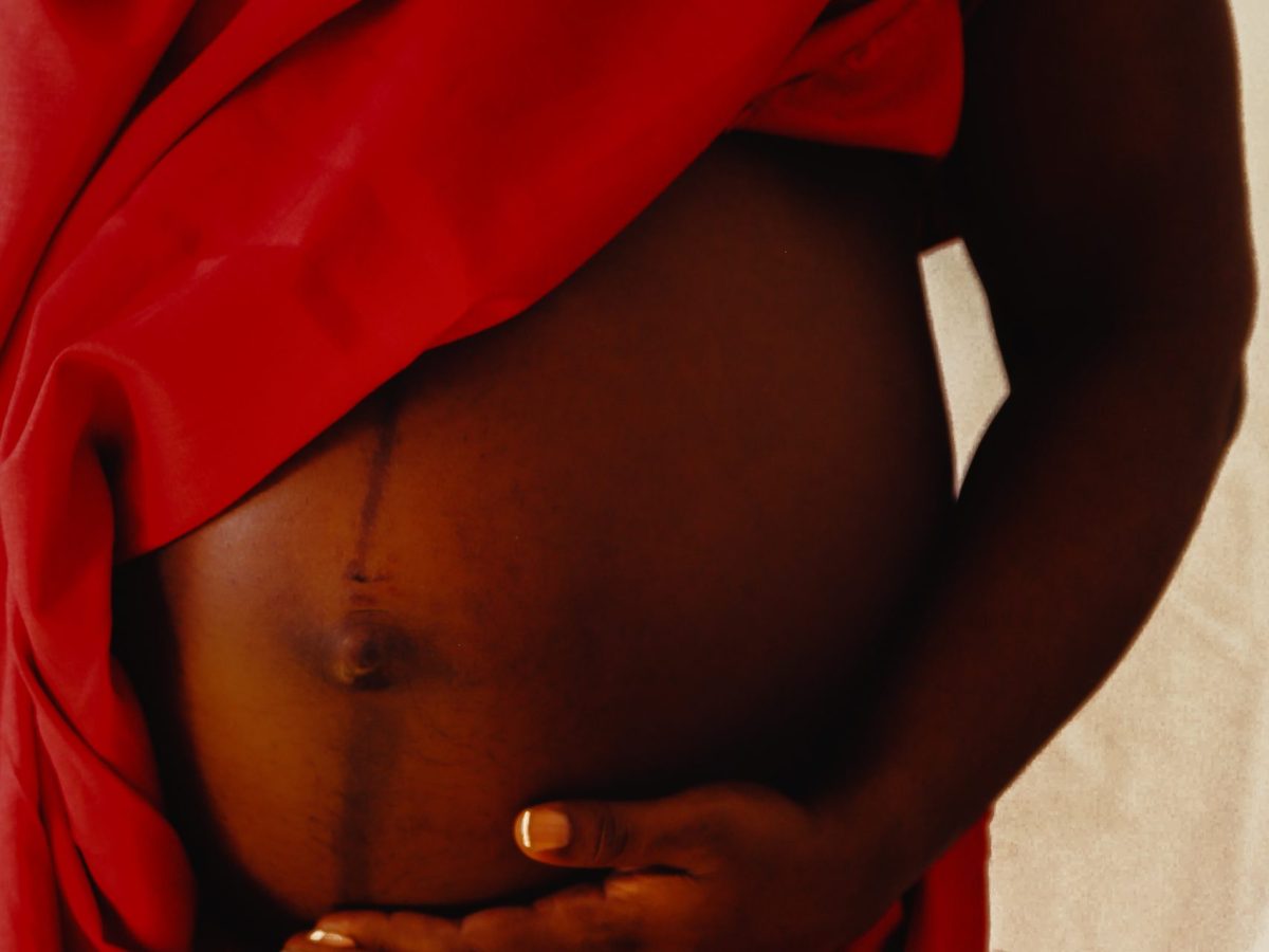 A pregnant person's belly. The person is draped in red. They have dark skin.