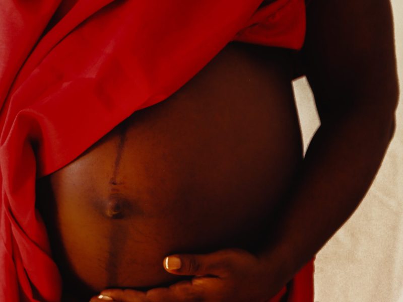 A pregnant person's belly. The person is draped in red. They have dark skin.