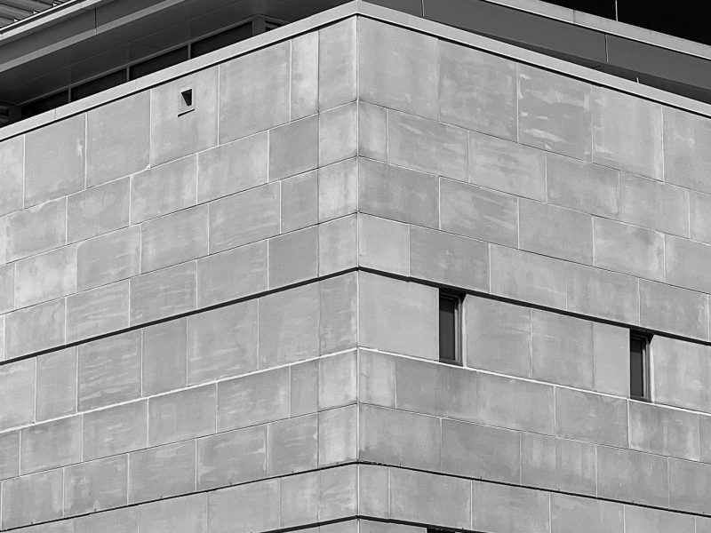 Black and white image of the Youth Detention Center in Baltimore City. The image is of a corner of the building. Tiny rectangular windows can be seen on the right hand side of the building