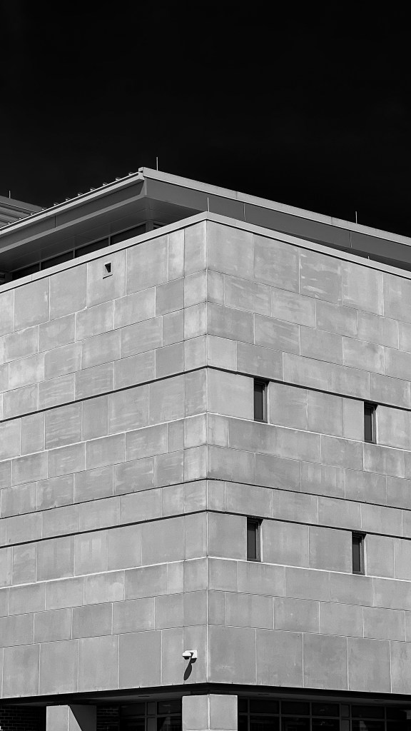 Black and white image of the Youth Detention Center in Baltimore City. The image is of a corner of the building. Tiny rectangular windows can be seen on the right hand side of the building