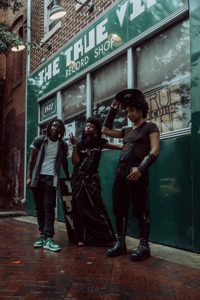 Three members of BLKVAPOR are pictured outside of True Vine Records. All three have brown skin. True Vine is green.