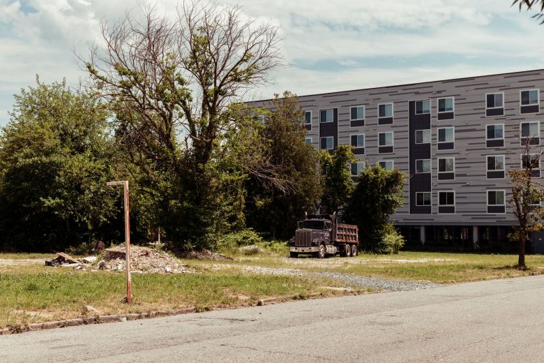 A color photo of an abandoned lot in Poppleton, with Center/West apartments in the background, a pile of rubble and a dump truck in the foreground.