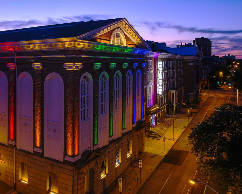 A photo of Baltimore Center Stage. It is lit up in rainbow colors.