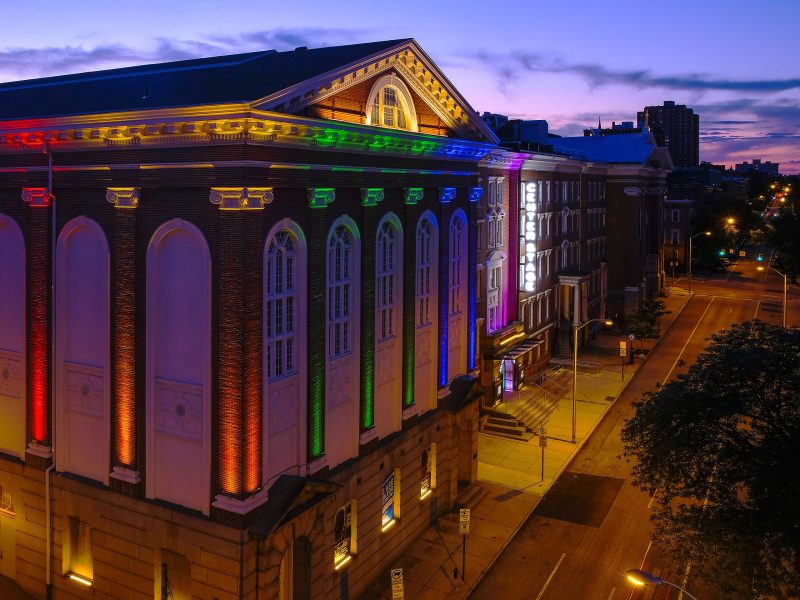 A photo of Baltimore Center Stage. It is lit up in rainbow colors.