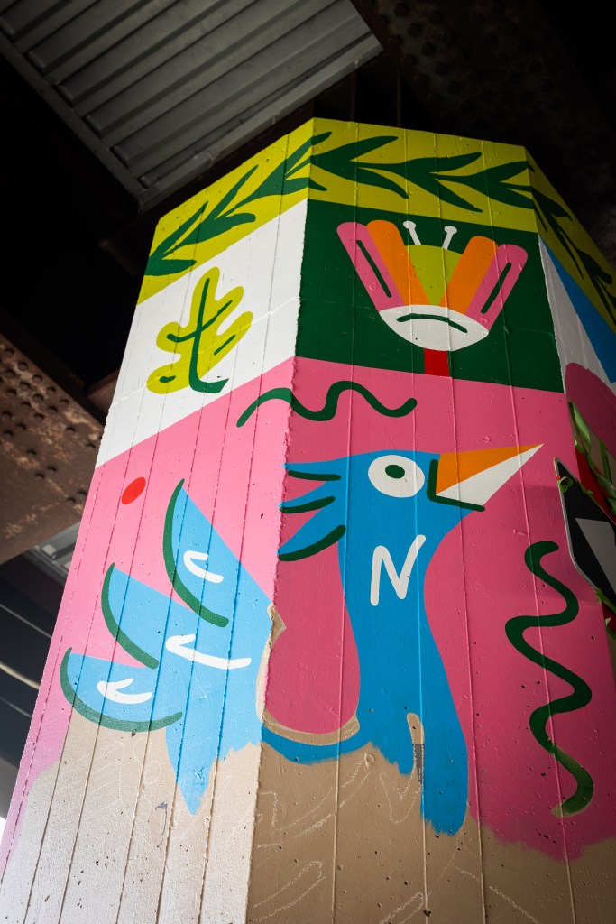 An in-progress mural featuring bright, geometric patterns and a stylized blue heron bird.