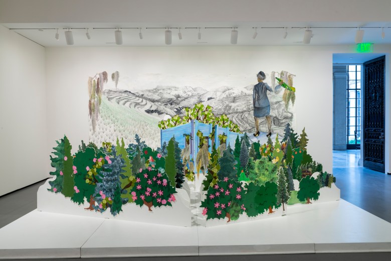 A large scale artwork installed in the Baltimore Museum of Art, it has rows of green plants cut out of materials, in the background there is a large drawing.