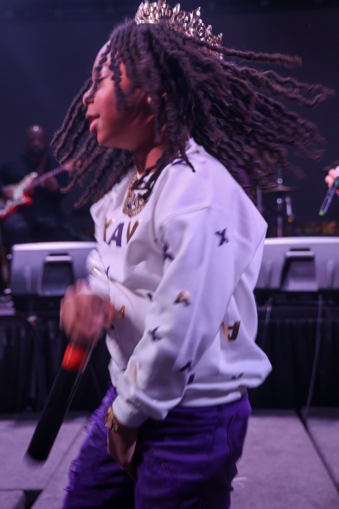 Photograph of a young person rapping, wearing a crown. 