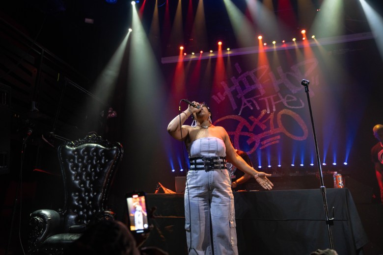 Omnia performs at a hip-hop showcase. She has brown skin and is holding a microphone .