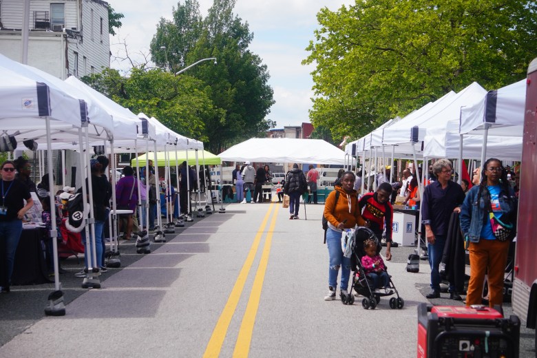 A photo of white tents on either side of a street. People stand at many of the tents. 