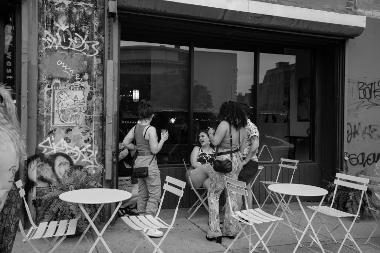 A group of people talk and laugh outside of Club Car. One is seated and three others are standing around them.