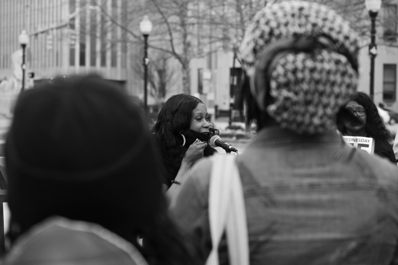 A woman speaks into a microphone with other supporters surrounding here
