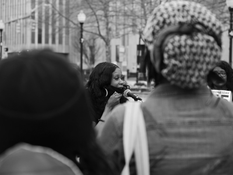 A woman speaks into a microphone with other supporters surrounding here