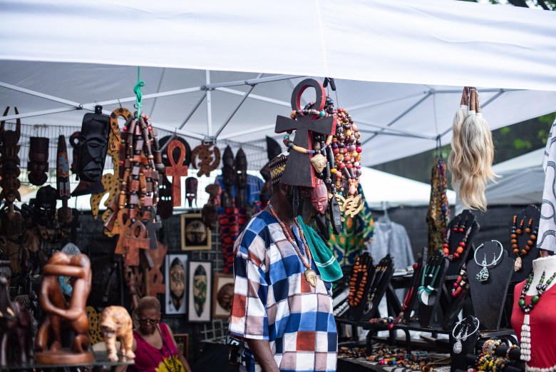 A man stands amid various decorations, beads, figurines, and other wares for sale.