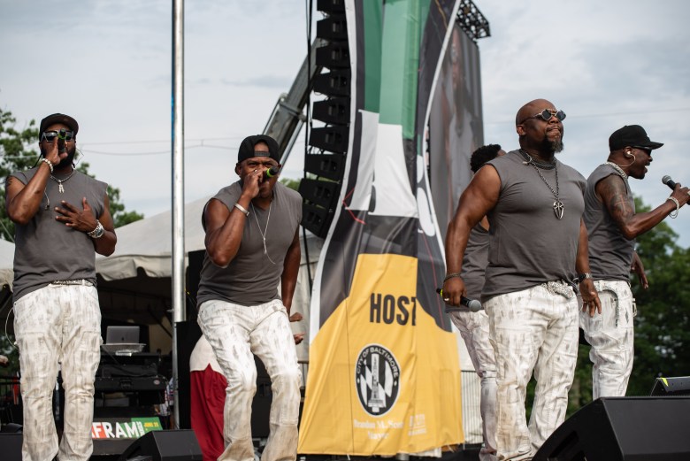 A group of men perform on stage. They all are wearing dark colored tops and light colored pants.