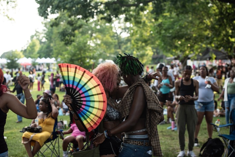 A couple dances close to each other. One holds a rainbow fan.