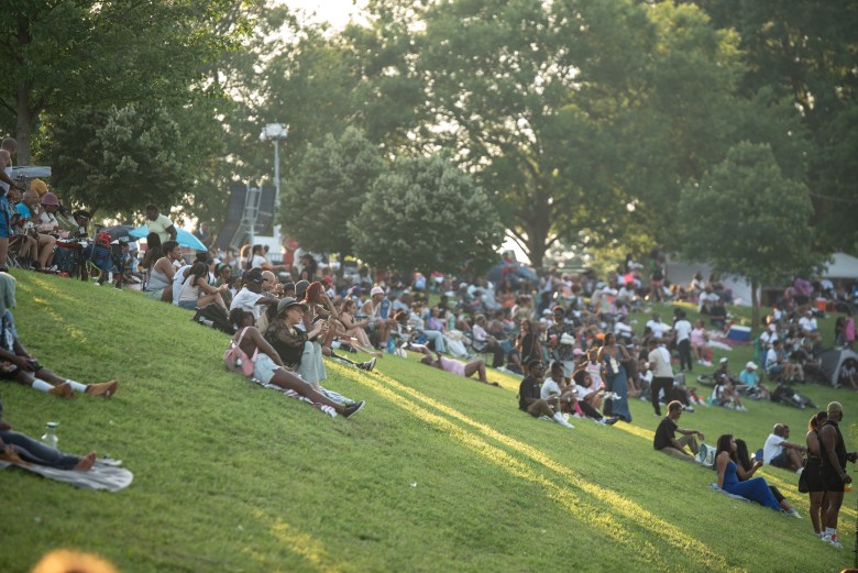 A photo of a crowd of people who are sitting on a grassy hill.