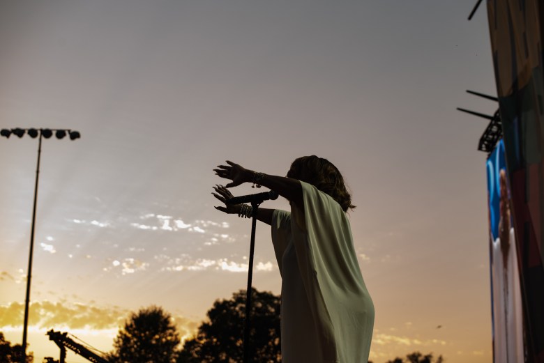 A woman performs with her arms raised as the sun sets.
